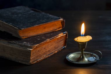 Geceleri karanlık odada, eski kitapların yanında, bronz şamdanda yanan mum, ahşap masanın üzerinde, kapat. İki kitabın yanında mum yakan klasik bir hayat.