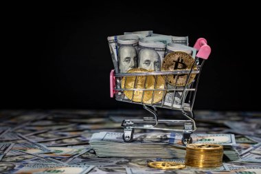 Şifreli altın Bitcoin sikkeler ve 100 dolarlık banknotların arka planında küçük bir alışveriş arabasında dolar, yakın plan. Dijital para ve bitcoin kavramı