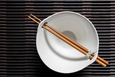 Tahta çizgili tepside boş bir çorba kasesinin üzerinde duran bir çift çubuk. Yaklaş, üst manzara.