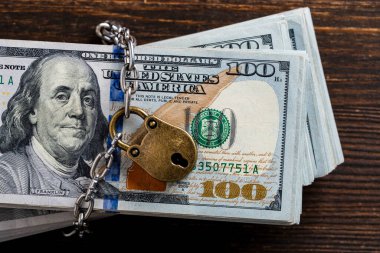Metalik zincir ve asma kilit Amerikan 100 dolarlık banknotlar, yakın çekim, üst manzara. İş güvenliği ya da finansal koruma ya da kısıtlama erişimi. Asma kilitli bir yığın para.
