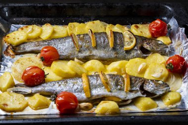 Fırında iki alabalık, patates dilimleri, limon, domates ve baharat, yakın çekim.