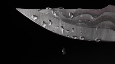 Siyah arka planda izole edilmiş sahte el yapımı bıçaklara su damlaları, yakın plan. Su bıçağa sıçrıyor.