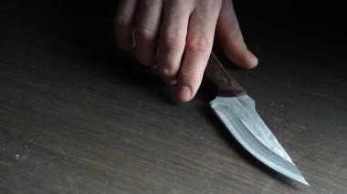 Adamın eli tahta masadan sahte keskin bir bıçak alır, yakın plan. Parlak bıçaklı demir bıçak erkeklerin elinde.