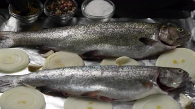 Aşçı, fırında pişirmek için hazırlanmış iki alabalık leşine baharat serpiyor.