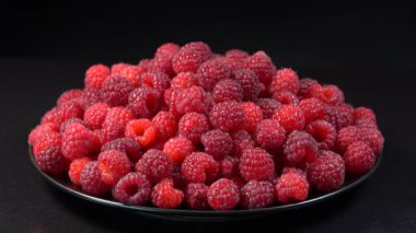 Taze, olgun, sulu ahududu arkaplan, böğürtlenleri kapat, dönüşümlü 4k. Yemek arkaplanı. Gastronomi konsepti, organik gıda. Siyah arkaplanda kırmızı ahududu tabağı