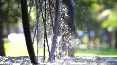 Güneşli bir günde Batumi şehrinde su sıçrayan güneş ışığına karşı güzel bir çeşme ve bisiklet tekerleği, Georgia. Ağır çekim, yakın çekim.
