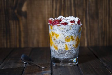 Bardakta taze ahududu ve ahşap arka planda portakal dilimleri olan sağlıklı chia pudingi, yakın plan, kopyalama alanı. Hindistan cevizi sütünde Chia tohumları, böğürtlen, meyve ve bal, masada kahvaltı için.