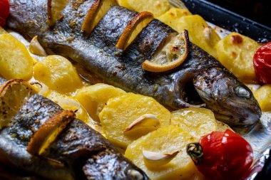 Fırında iki alabalık, patates dilimleri, limon, domates ve baharat, yakın çekim.