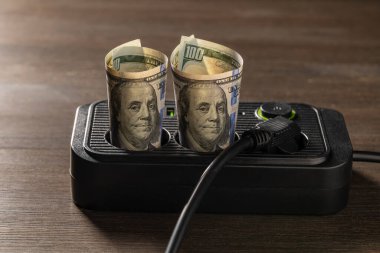 Tahta arka planda Amerikan Doları banknotları olan prizler, yakın plan. Enerji maliyetleri ve elektrik faturası kavramı