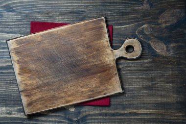 Ahşap mutfak masasındaki kırmızı peçetenin üzerine boş kesme tahtası, üst manzara, kapat, kopyala