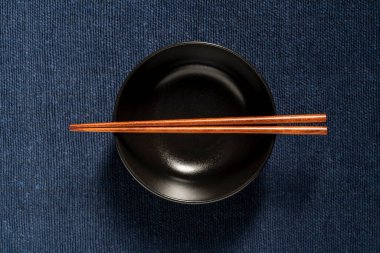 Mavi kumaş arka planda boş bir siyah çorba kasesinde duran bir çift tahta çubuk, yakın plan, üst manzara