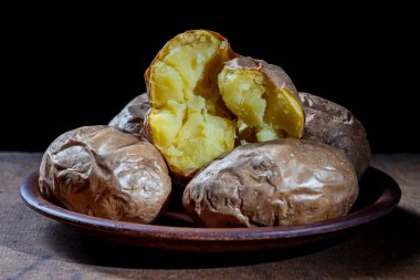 Kil tabakta bütün patatesler, yakın çekim. Siyah arka planda basit Ukrayna yemekleri. Yemekte patates var.