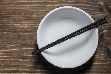 Bir çift siyah yemek çubuğu boş beyaz bir çorba kasesinin üzerinde, ahşap masada, yakın plan, üst manzara