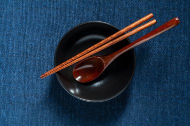 Bir çift ahşap yemek çubuğu ve kaşık mavi kumaş arka planda boş bir çorba kasesinde yatıyor.