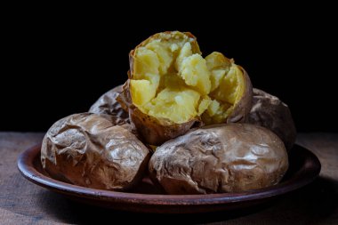 Kil tabakta bütün patatesler, yakın çekim. Siyah arka planda basit Ukrayna yemekleri. Yemekte patates var.