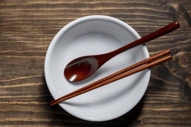 Bir çift ahşap yemek çubuğu ve kaşık boş bir çorba kasesinin üzerinde, ahşap masanın üzerinde, yakın plan, üst manzara