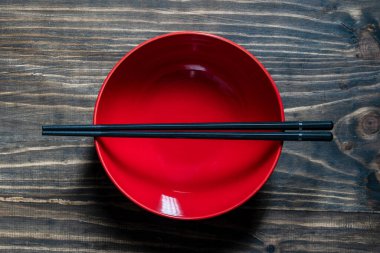 Bir çift siyah yemek çubuğu boş bir kırmızı çorba kasesinin üzerinde, ahşap masada, yakın plan, üst manzara