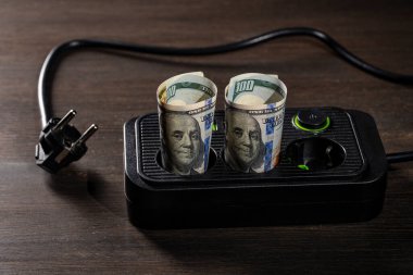 Tahta arka planda Amerikan Doları banknotları olan prizler, yakın plan. Enerji maliyetleri ve elektrik faturası kavramı