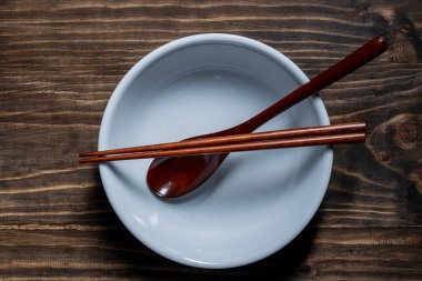 Bir çift ahşap yemek çubuğu ve kaşık boş bir çorba kasesinin üzerinde, ahşap masanın üzerinde, yakın plan, üst manzara