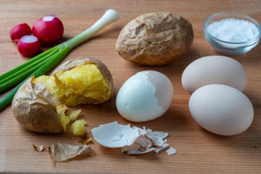 Kırık patatesler, haşlanmış yumurtalar, yeşil soğanlar ve turplar ahşap bir masada, yakın çekim. Basit çiftlik yemekleri.