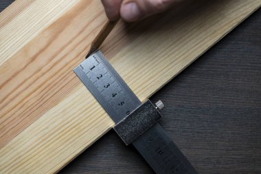 Marangoz çelik cetvel işaretleme ya da şablon için limitli blok, yakın çekim, üst görünüm. İşçi el metal bir cetvel tutuyor ve tahta bir tahta üzerinde kurşun kalemle izler var.