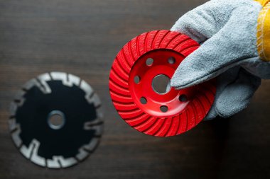 İnşaat eldivenleri içinde çalışan işçi, çimento öğütmek için yeni bir kırmızı elmas disk tutuyor.