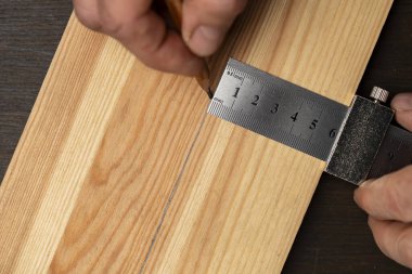 Marangoz çelik cetvel işaretleme ya da şablon için limitli blok, yakın çekim, üst görünüm. İşçi el metal bir cetvel tutuyor ve tahta bir tahta üzerinde kurşun kalemle izler var.