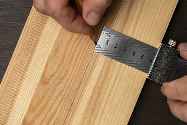 Marangoz çelik cetvel işaretleme ya da şablon için limitli blok, yakın çekim, üst görünüm. İşçi el metal bir cetvel tutuyor ve tahta bir tahta üzerinde kurşun kalemle izler var.