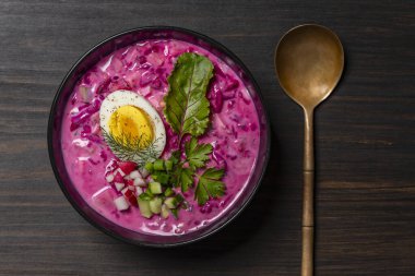 Soğuk pancar çorbası, pancar, salatalık, turp, haşlanmış yumurta ve ekşi kremadan yapılan geleneksel Ukrayna yemeği. Lezzetli soğuk yaz pancar çorbası siyah kasede masada, yakın plan, üst manzara