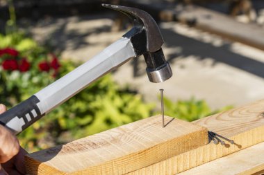 İşçi çekiç kullanıyor. Tahtaya metal çivi çakıyor. Yaklaş. Çalışmak için el aleti. Çok işlevli şok geçirmez çelik çekiç ve çivi.