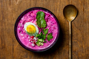 Soğuk pancar çorbası, pancar, salatalık, turp, haşlanmış yumurta ve ekşi kremadan yapılan geleneksel Ukrayna yemeği. Lezzetli soğuk yaz pancar çorbası siyah kasede masada, yakın plan, üst manzara