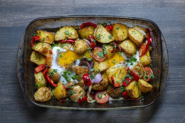 Cam bir kabın içinde yumurta ve fırında sebze, üst manzara, yakın çekim. Patates, domates, kırmızı biber, fırında pişmiş soğan ve yumurta. Yazın sebzelerden elde edilen basit kırsal yiyecekler.