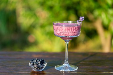 Böğürtlenli buzlu meyve suyu, klasik kristal camla ahşap masada, yaz bahçesi arka planında, yakın plan. Sağlıklı beslenme kavramı. Yabanmersini, muz, bal ve yoğurttan meyve suyu.