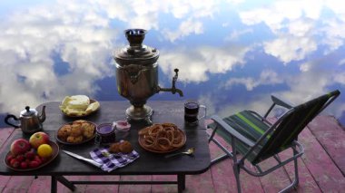 Ukrayna 'da, ormandaki sakin su gölünün yanındaki masada beyaz duman ve yiyecek bulunan klasik metal çay semaveri. Doğa gıda konsepti