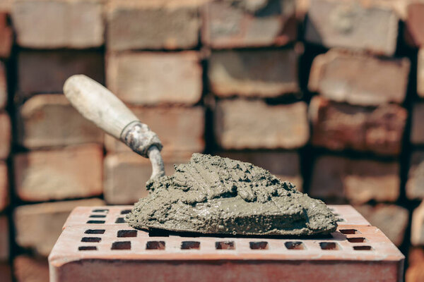 Цементная смесь или раствор. Цементный порошок и лопатка на красном кирпиче на строительной площадке, крупным планом