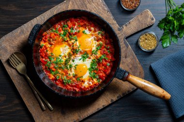 Shakshuka kahvaltıda kızartma tavasında, kapat. Haşlanmış yumurta, soğan, dolma biber, zeytinyağı, dökme demir tavada kırmızı domates ve maydanoz karışımı. Akdeniz mutfağı