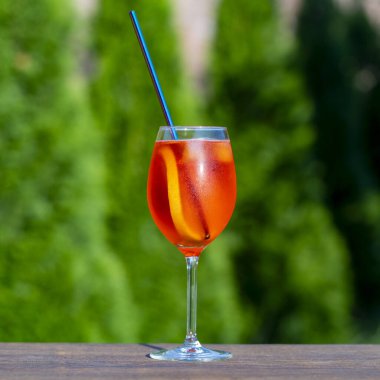 Aperol spritz kokteyli ve şarap kadehi, doğal bir arka plan. Klasik İtalyan aperatifi aperatif sprey kokteyli. Bir dilim portakallı. Kapatın. Yaz güneşli ferahlatıcı içecek
