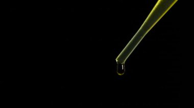 Cosmetic pipette with essential oil drops on black background, macro view. Concept of natural cosmetics or pharmaceutical medicines