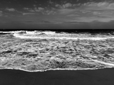 Çarpıcı bir siyah beyaz fotoğraf fırtınalı bir gökyüzünün altında şiddetli bir şekilde düşen fırtınalı okyanus dalgalarını yakalıyor.