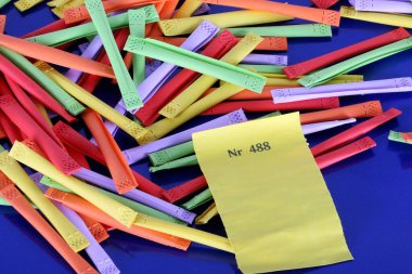 a heap of colorful tombola tickets with a yellow winning number are lying on a blue reflection ground