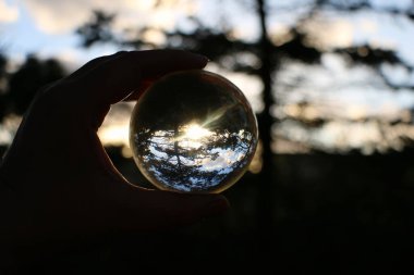 Bir insan elinin cam bir topu tutarken ve gün batımını seyrederken.