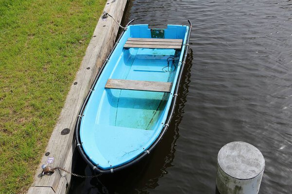 small old broken turquoise boat is moored in the small river at the edge and has water in the boat