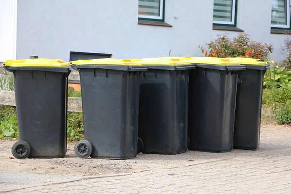 Many garbage cans for plastic waste with yellow lids stand on the side of the road and wait to be emptied