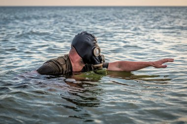 Siyah gaz maskeli bir adam denizde yüzer. Kıyametsel tema gönder