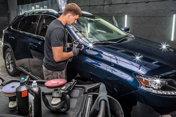 Professional car service male worker, with orbital polisher, polishing blue luxury car hood. Car detailing