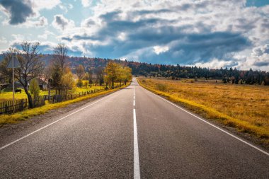 Landscape with empty asphalt road with cloudy sky and sunlight in autumn mountains