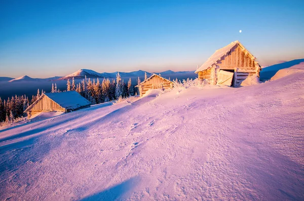 Beautiful winter landscape with abandoned cabins at sunrise or sunset in snowy Carpathian mountains