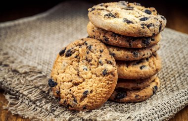 Stack of delicious cookies with pieces of chocolate on burlap napkin clipart