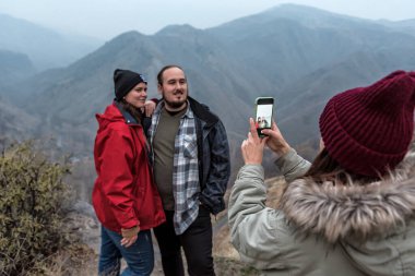 Turist kadın, arkadaşlarının fotoğraflarını akıllı telefon kamerasıyla dağların arka planında çekiyor..