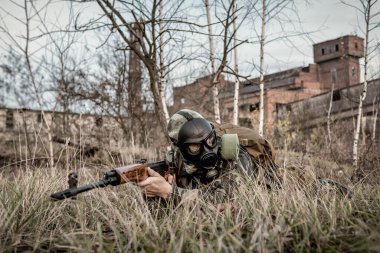 Gaz maskeli, tüp tüfekli hayatta kalan asker radyoaktif bölgede yatıyor. Askeri tema